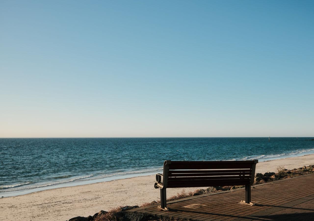 Parkbank an einem ruhigen Strand mit Blick auf das Meer - Symbolbild fuer den Wegzug und neue Horizonte